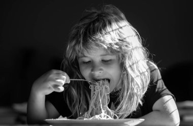 Küçük çocuk mutfakta spagetti yiyor. Bulanık arka planda yemek yiyen çocuk. Aç küçük çocuk yemek yiyor. Çocuklar için ev yemeği