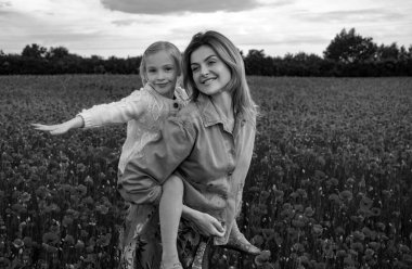 Anne ve kızı gelincik çayırında sarılıyorlar. Anne ve kız gelincik çiçekleriyle tarlada dinleniyor, sırtına biniyor. Mutlu annelik