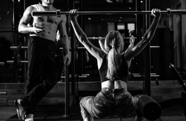 Spor salonunda halterle çalışan güçlü bir kadın. Halterli kadın çalıştıran kaslı antrenör.