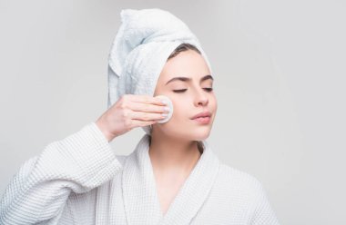 Gri arka planda Pamuk Pedle yüzünü yıkayan Güzel Genç Kadın 'ın yakın çekimi. Gözler kapalı.