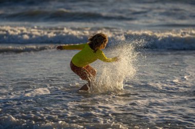 Heyecanlı çocuk yaz denizinde su sıçratarak oynuyor. Yaz tatili. Çocuk denizde dalgalarla oynuyor. Küçük çocuk denizde oynuyor ve su damlaları sıçrıyor. Çocuk denizde su sıçratmaca oynuyor. Yaz tatili