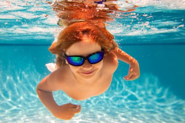Yüzme havuzunda su altında bir çocuk. Çocuk su altında yüzüyor. Yüzme havuzunda su sıçratan çocuk. Aktif çocuklar sağlıklı yaşam tarzları, su altında yüzme. Çocukla yaz tatili. Çocuk su oyunu