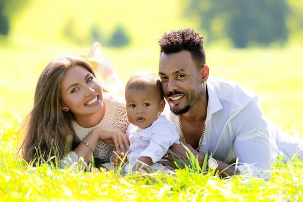 Mixed race family outdoor portrait. Parents and child family portrait in park. Happy African American dad and mixed race baby spend time together. Happy mixed race family. Young interracial family
