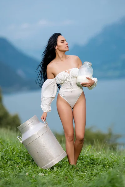 Sensual woman with milk outdoor. Milky Alps. Natural organic raw milk. Girl with a bottle of fresh milk in the Alpine village. Beautiful woman enjoys milk on alpine village. Milking farm concept. Sexy