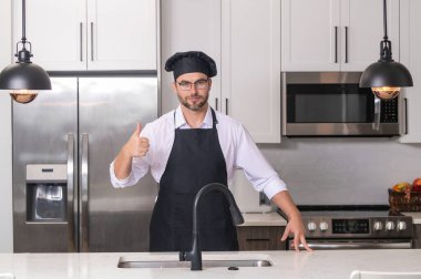 Üniformalı yakışıklı aşçı mutfakta yemek yapıyor. Restoran menüsü konsepti. Fırıncı üniformalı İspanyol adam. Aşçılık ve aşçılık. İş üniformalı, siyah önlüklü, şef şapkalı bir aşçı.