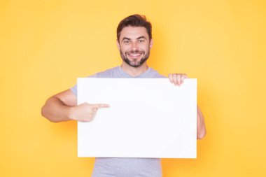 Boş tahtayı tutan ve tekneyi işaret eden mutlu adam. Telif uzayı olan boş bir tahta gösteriyor. Fikir ve teklif. Reklamınız. Metin ve maket için boş alanı olan boş reklam panosu