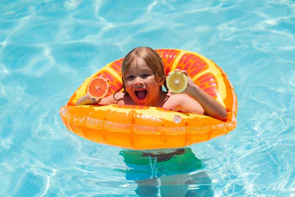 Kid with orange in the pool. Summer fruits. Cute little boy in pool on summer day with orange. Outdoor summer activity for children. Summer kids vacation. Child boy swimming in pool
