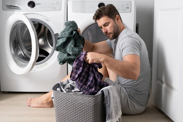 Man with clothes near washing machine. Laundry cleaning. Housework, homework, male housekeeper. Husband man doing laundry at home. Washer and dryer at home
