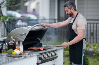 Barbekü, ızgara, dışarıda barbekü. Barbekü kızarmış balıklı bir adam. Izgara ve barbekü konsepti. Mangal ve ızgara. Barbeküde balık somonu hazırlayan adam. Şef ızgara deniz ürünleri pişiriyor.