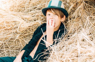 Küçük çocuk doğal ürünler tanıtır. Sonbahar adil mutlu bir çocuk. Bir saman yalan neşeli bir çocuk portresi. Sarışın çocuk saman arka plan üzerinde yatıyor ve bir elma yiyor