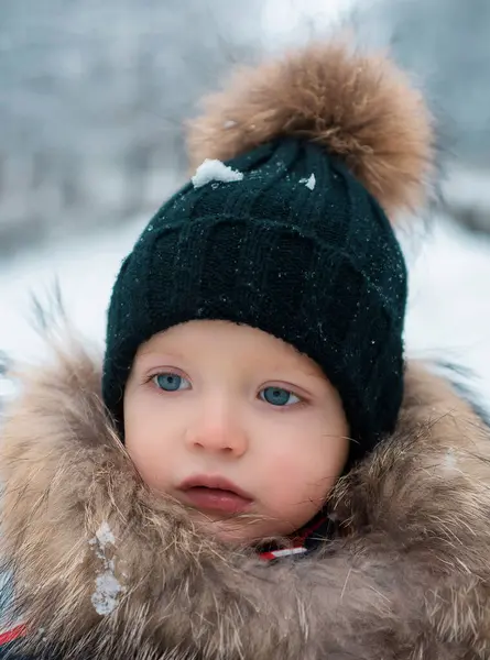 Cute little boy in winter clothes. Kid in winter clothes walking under the snow. Cute little boy. Portrait of a little boy in the snow. Charming boy. While having fun outdoors