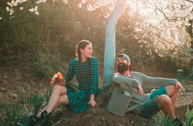 Bahar bahçesinde çimlerde oturan arkadaşlar. Baharda bahçe aletleri ile gençlik. Sıkı çalışmadan sonra dinleniyor.