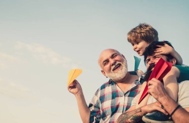 Erkek nesli. Mutlu çocuk oyuncak kağıt uçakla oynuyor yaz gökyüzü arka planında. Babasıyla dışarıda oynayan sevimli bir oğlu var. Mutlu bir aile. Baba oğul büyükbabayla mutlu bir aile.