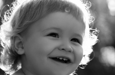 Küçük sarışın bir erkek bebeğin yakın portresi. Komik çocuklar güneşli bir günde açık havada yüzlerini kırptılar. Çocuklar gülümsüyor, sevimli gülüyor.