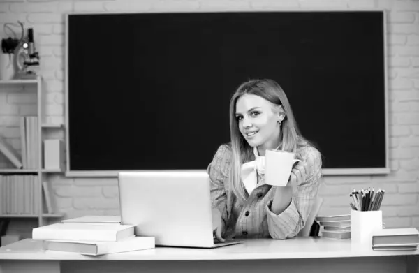 Portrait of smiling young college student drinking coffee or tea, studying in classroom