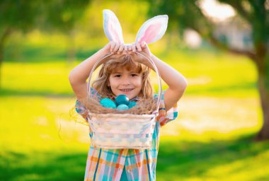 Çocuklar için mutlu Paskalyalar. Tavşan kulaklı çocuk dışarıda paskalya yumurtası avlıyor. Çocuk parkta paskalya geçiriyor. Paskalya yumurtası avı
