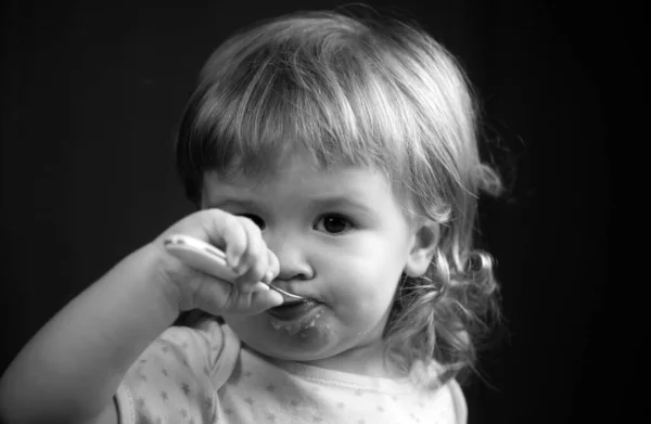 Baby eating with dirty face. Cheerful smiling child child eats itself with a spoon Baby eating with dirty face. Smiling little child eating food on kitchen. Kid hungry