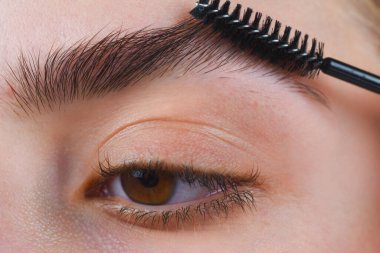 Kaş şekillendirme. Kadının kaş makyajı yaptırmasına yakın çekim. Kaşlarını tarama makrosu. Mükemmel bir kaş şekli, kahverengi göz farı ve uzun kirpikleri. Güzel kaşlı kız.