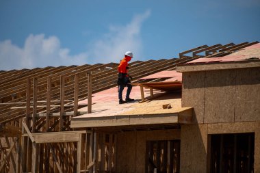 Çatı katı. Çatı inşaatı. Roofer hava çivisi kullanıyor. İnşaat binasının altındaki yeni çatının çatı kiremitleri. Binanın çatısını onarıyorum. Çatıları onarmak, çatı döşemek, evi yenilemek. Çerçeve çatısı