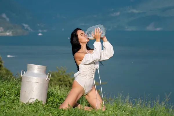 Woman drink milk at Swiss Alps in Switzerland. Young woman drinking milk from bottle. Milking day. Sexy milky mouth with splash. Model drink Milk at Alpine meadow. Woman body with face splashed milk
