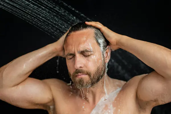 Middle aged man washing hair in bath. Guy bathing shower head in bathtub. Face in foam in shower. Bathing man taking shower. Close up guy showering. Shower concept. Man is under water drops in showers
