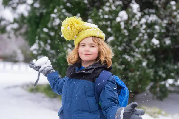 Child play with snow in winter park. Kids with first snow. Child winter holiday. Smiling boy playing with snow in winter park. Portrait of a little kid in knit hat throw snowballs. Funny kids in snow