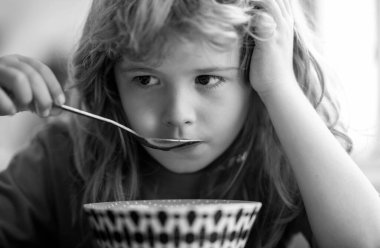 Evde kahvaltı yapan çocuk portresi. Küçük tatlı bir çocuğun portresi. Sarı saçlı. Tabak kaşığı yiyor.