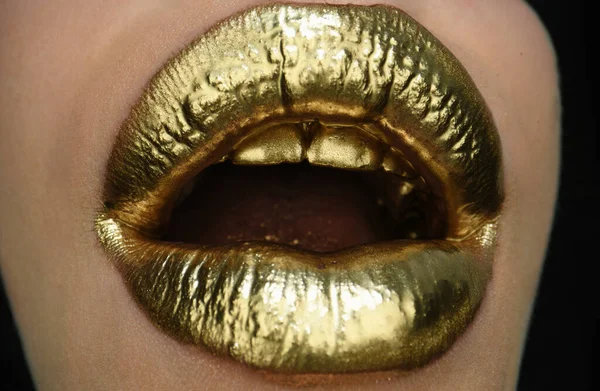Gold lips. Gold paint from the open mouth. Golden lips on woman mouth with make-up. Sensual and creative design for golden metallic