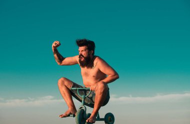 Çocuk bisikleti süren adam. Sakallı bir adamın dışarıda bisikletle eğlenen çılgın bir hippi portresi. Heyecanlı genç erkek küçük bir bisiklet sürüyor ve mutluluğu işaret ediyor.