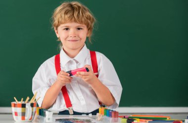 Okuldaki çocuk boyalarla resim çiziyor. Çocukların yaratıcılığı. Çocukluk eğitimi, çocukların sanatsal becerileri.