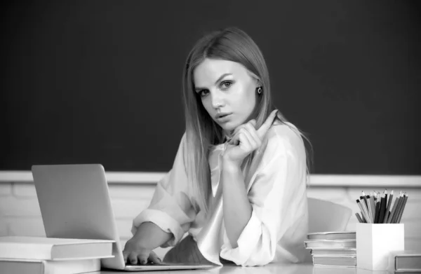 Portrait of young female college student studying in classroom on class with blackboard background. Beautiful caucasian female student is studying in college remotely, distance learning