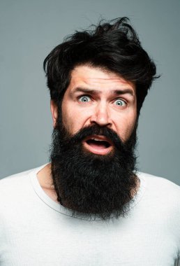 Şaşırmış yakışıklı adam. Şaşırmış erkek model, şaşırmış surat ifadesi, şaşırmış surat. Duygular insanlar konsepti. Gri arka planda poz veren sakallı hippi