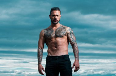 Seksi bir adamın baştan çıkarıcı yüzü. Maço kendinden emin görünüyor. Dramatik gökyüzünde açık hava erkek portresi