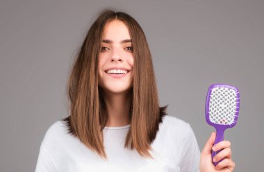 Kadın tarak ile saç stili yapıyor. Stüdyoda sağlıklı ve parlak saçları olan güzel bir genç kadın. Saçını tarayan genç kadına yaklaş.