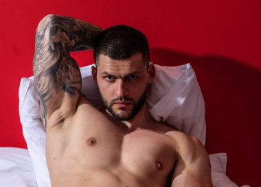 Muscular man lying shirtless in bed. Young handsome man resting on the bed at home. Guy with thletic flexing muscles on bed. Sexy young handsome naked man on bed. Seductive gay