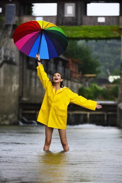 穿着雨衣的有趣而兴奋的女人拿着雨滴雨伞 雨季穿雨衣的女孩在瀑布下滴水 拿着雨伞的女人夏天的雨雨天 — 图库照片