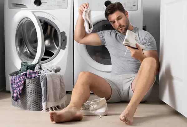 Man loading clothes into washing machine in laundry room. Middle age man putting laundry in to washing machine scared and amazed with open mouth for surprise, disbelief face with dirty clothes