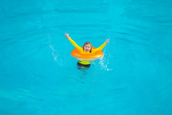 Child play in pool on inflatable ring. Kid with inflatable ring in swimming pool. Child water toys. Children play in tropical resort. Child in swiming pool. Kid floating in sea