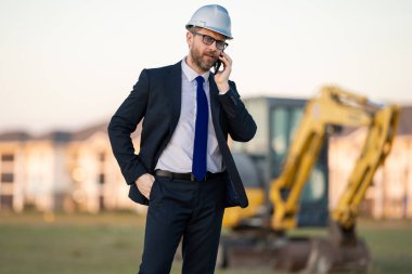 İnşaat işletmecisi ya da şantiye müdürü. İnşaat müdürünün portresi, kazıcının yanında şapka ve takım elbise giymiş. İnşaat yöneticisi veya denetçisi ile yenileme