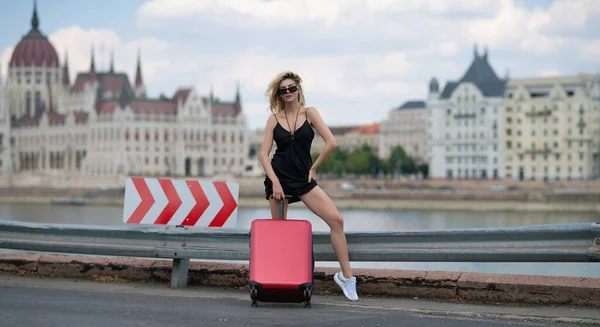 Fashion woman with luggage, suitcases going on vacations. Travel lifestyle. Tourist girl with travel bag travelling on budapest city street outdoor