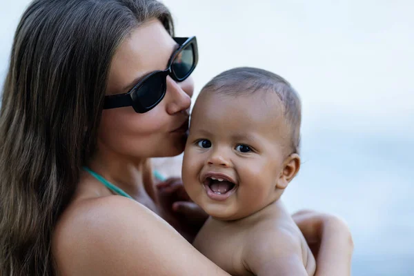 Close up portrait of mother kissing multiracial baby. Mom kiss Biracial child. Closeup face of Mother with Biracial baby kissing outdoor. Tender moms kiss. Biracial or multiracial baby and mom kissed