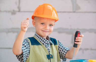 Turuncu koruyucu kasklı küçük bir çocuk ve yenileme aletleri var. Gülümseyen mutlu çocuk inşaatçısı ve tamircisi