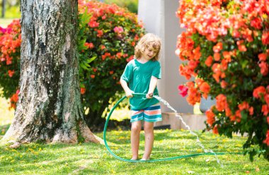 Çocuklar bahçede su hortumuyla oynuyorlar. Açık hava çocukları yaz eğlencesi. Küçük çocuk arka bahçede su hortumuyla oynuyor. Çocuklar için parti oyunu. Sıcak güneşli bir gün için sağlıklı aktivite