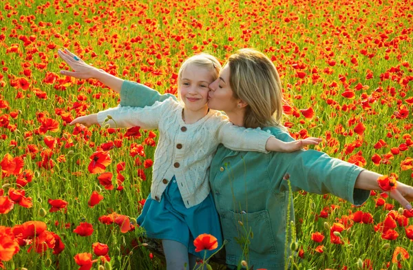Happy spring family. Carefree mom with a child girl in a field of red poppies enjoys nature. Mother and little daughter in the poppy field. A young woman with her daughter in in a poppy field