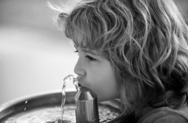 Parktaki çeşmeden su içen bir çocuk. Susamış çocuk