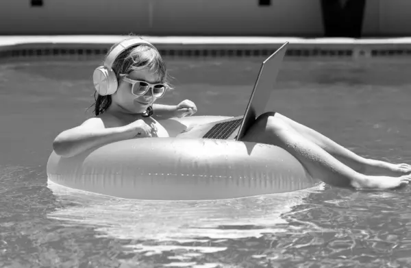 Kids working with laptop on summer vacation holidays. Little freelancer using computer, remote working in swimming pool. Summer travel and business concept