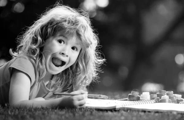 Excited kid painting in spring nature. Portrait of smiling happy kid enjoying art and craft drawing in backyard or spring park. Children drawing draw with pencils outdoor