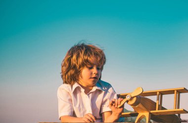 Tahta oyuncak uçakla oynayan çocuk pilot olma hayali kuruyor. Çocuk rüyaları. Ahşap uçaklı çocuk pilot.