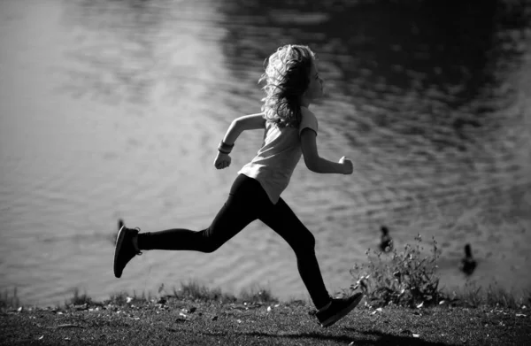 Child runners run in park. Boy running in the park in summer in nature. Outdoor sports and fitness. Kids running on green meadow against sea or lake