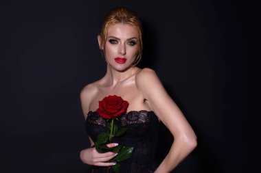 Beauty studio portrait. Beautiful model with red rose flower, isolated on black studio background. Charming young girl with perfect makeup